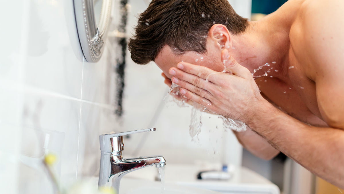 Seorang pria sedang mencuci wajah di wastafel tanpa mengenakan atasan